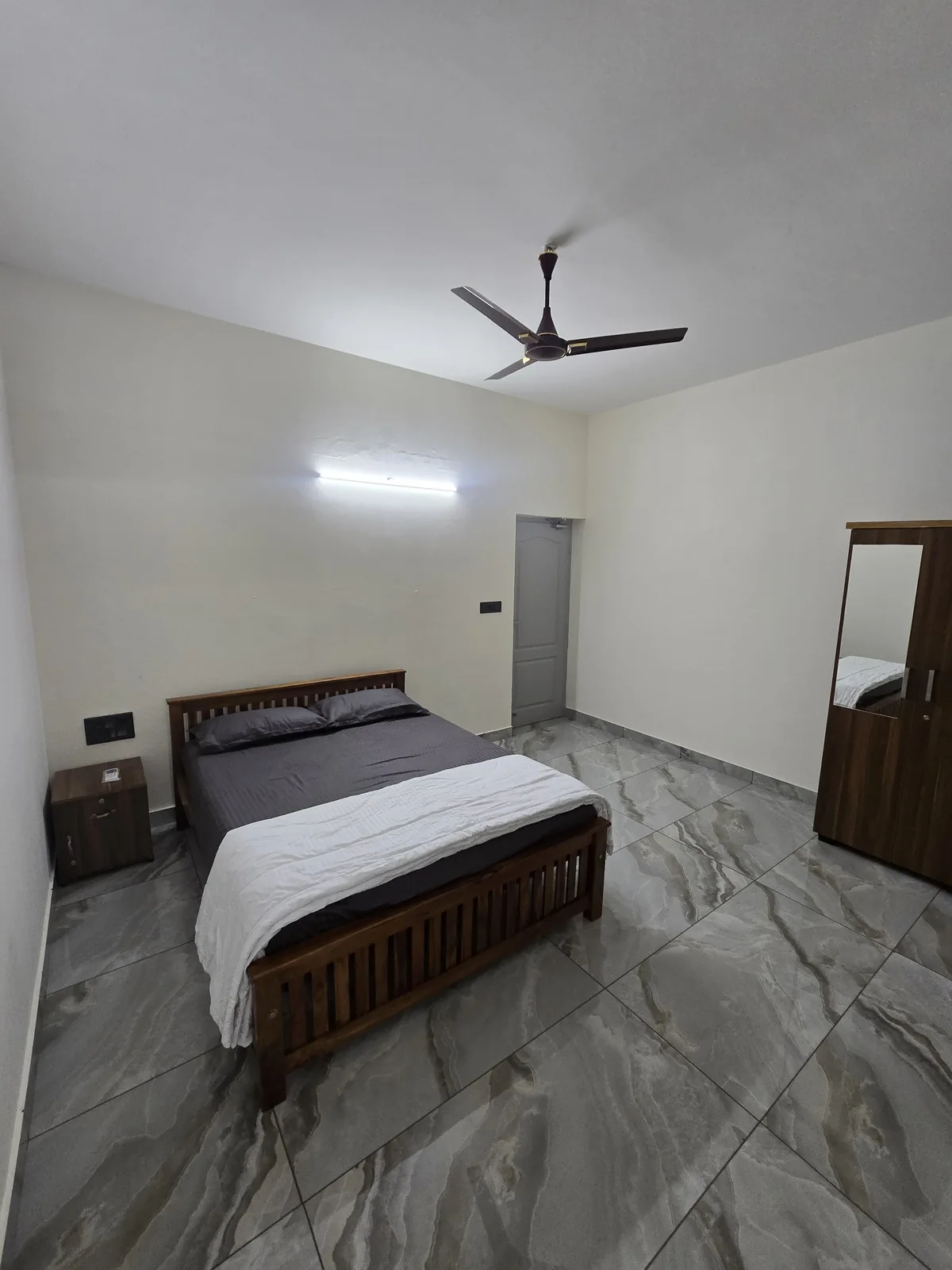 Guest bedroom with wooden bed and tiled flooring at Grey Oasis in Thrissur